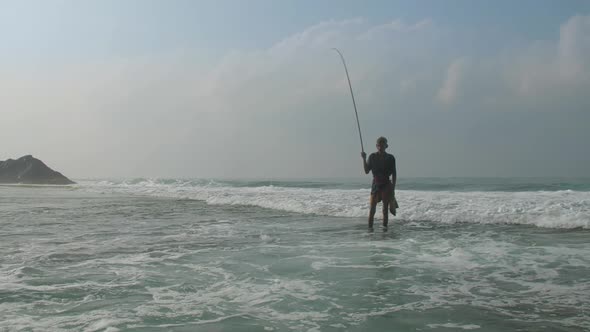 Fisherman Stands in Foaming Ocean Water Under Cloudy Sky