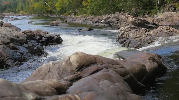 Water Flowing Down Rapids Into Wider Stream Beside Forest