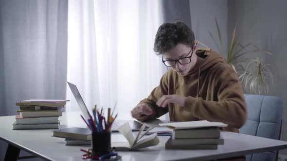 Side View of Young Genius in Eyeglasses Typing on Laptop Keyboard and Writing in Workbook. Portrait