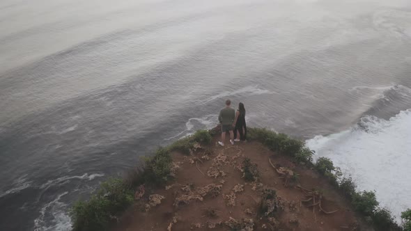 Drone View of Man and Woman Standing in Edge of Rock Looking at Sea