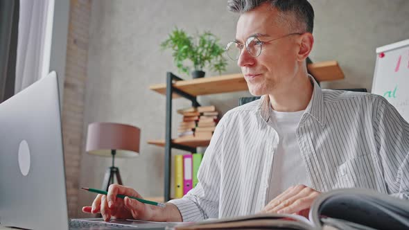 Mature Man Using Laptop Computer with Manual Book Feeling Stressed of Modern Gadgets Taking Off