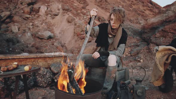 Dystopian Woman Sitting by Campfire in Garbage Can