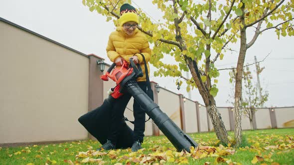 Smiling Boy in Reading Glasses and Yellow Jacket Helping at Backyard on Fall Day