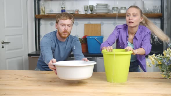 Young Couple with Plastic Basins Collecting Drops of Water Falling From Kitchen Ceiling