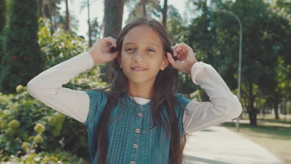 Portrait of Girl Combing Straight Hair Looking Into Camera Outdoors