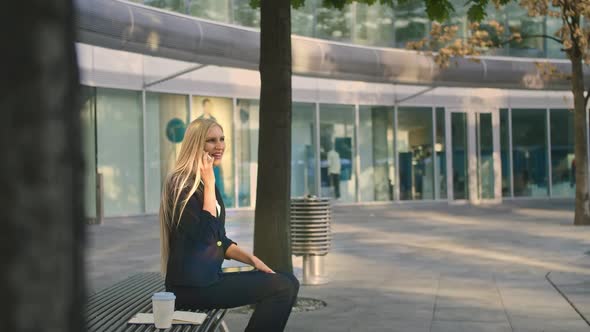 Business Woman Speaking on Phone and Waving with Hand. Elegant Modern Young Lady Sitting on Bench