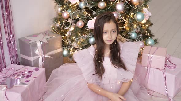 Girl in a Pink Dress Sits at Christmas Tree and is Photographed By a Photographer in the Studio