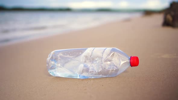 Slow motion close-up of plastic bottle being picked up from calm sandy beach. Water in background.