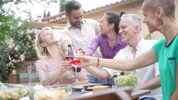 Friends Around Table at Home Garden for Dinner and Making a Toast with Rose Wine in Summer to