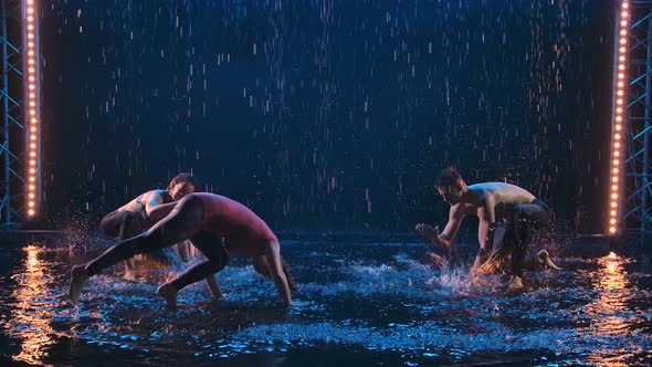 An Athletic Man and Two Young Women Practice Brazilian Capoeira Martial Art in the Rain in a Dark