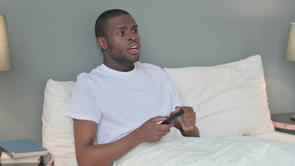 Young African Man in Bed Watching Television and Reacting to Loss