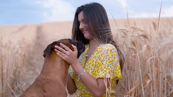 Cheerful young woman stroking and hugging her dog while they enjoy the day together in a wheat field