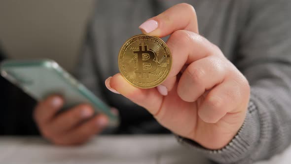 Woman Hand Holding Bitcoin and Phone Mining Bitcoins From Websites