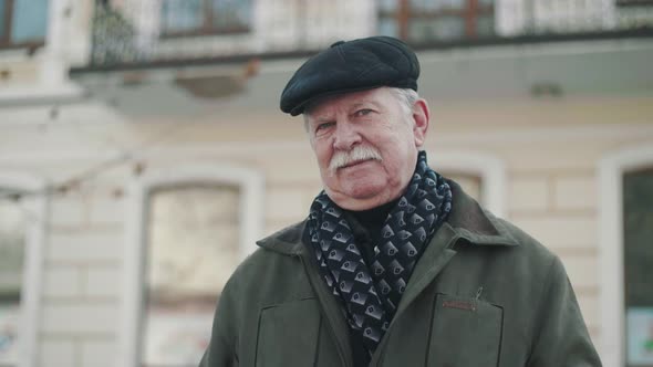 Optimistic White-haired Man in a Flat Cap Smiling at a Historic Building in Slo-mo   