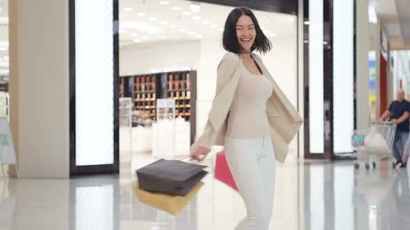 Woman in Soft Colored Jeans and Jacket Walking and Spinning at the Mall While Carrying Shopping Bags