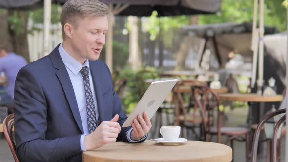 Online Video Chat on Tablet By Businessman Sitting in Outdoor Cafe