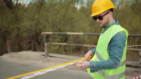 Bearded Engineer in Protective Helmet Tape Measure in Hands Measures Distance