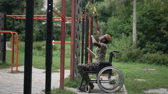 Side View Motivated African American Young Man in Wheelchair Stretching to Sports Equipment in