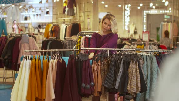 Woman Sorts Things Out on a Hanger in a Store