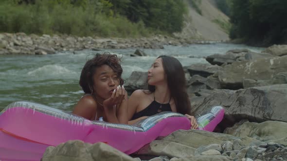 Pretty Multicultural Female Friends in Swimwear Enjoying Leisure on Air Mattress in Mountain River