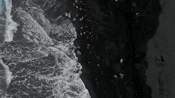 Aerial shot along the sea front on a black sand beach covered in icebergs.