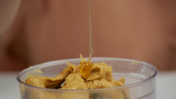 Adding honey to a peanut butter mixture in a blender.
