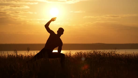 Silhouette of Young Sportive Man Practicing Yoga at Sunset