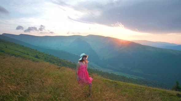 Young Woman in Red Dress Walking on Grass Field on a Windy Evening in Autumn Mountains