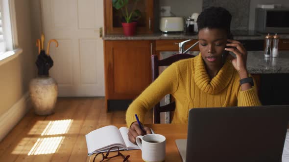 African american woman talking on smartphone and taking notes while working from home