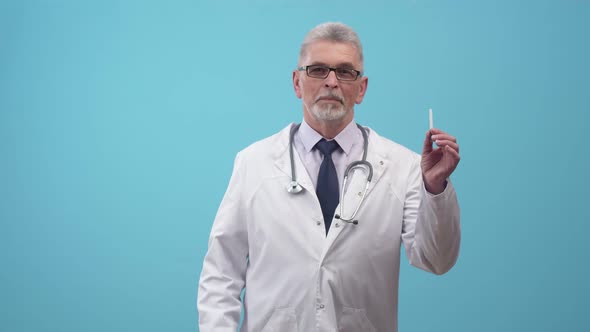 Man Doctor Holds a Cigarette in Hand and Negatively Moves Finger Looking at Camera on the Blue