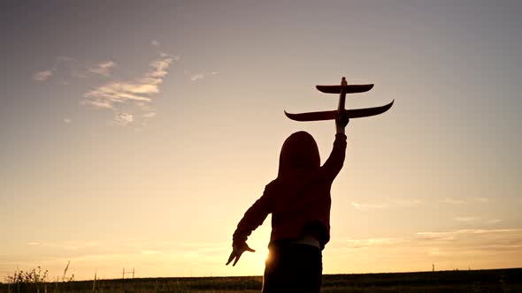 Silhouette of Happy Little Boy Running with Toy Plane or Aircraft on Sunset Sky Background