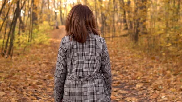 A Young Woman in Glasses and a Coat Walks in the Autumn Forest. Yellow Leaves Around. Slow Motion