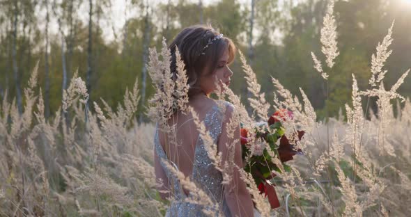 A Young Woman Dressed in a Gray Wedding Dress. She Has Flowers in Her Hand and Is in the Park