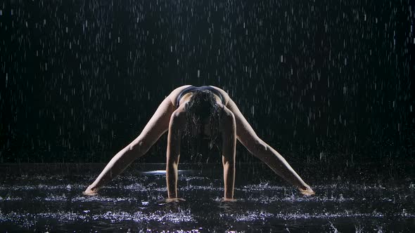 Slender Woman Wet From the Rain Practices Yoga Asanas in a Dark Studio. The Sexy Body Is Covered