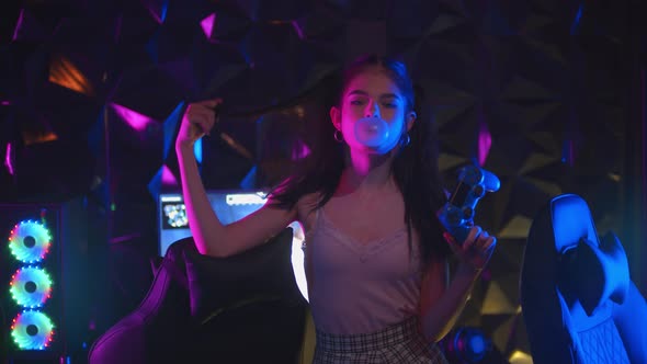 Young Sexy Woman with Ponytail Holding a Joystick in Neon Gaming Club and Blows a Bubble Gum