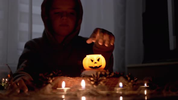 Hooded Shaman Boy Conjures Over Pumpkin Candle in Dark Halloween Room