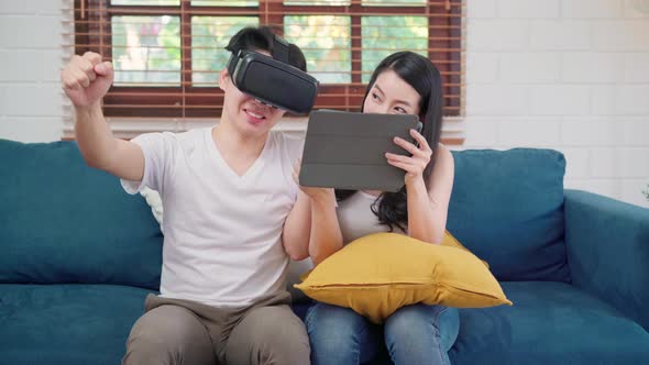 Asian couple using tablet and virtual reality simulator playing games in living room.