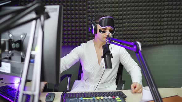 Radio Host in Sleep Mask and Cosmetic Patches Drinking Coffee on Broadcast