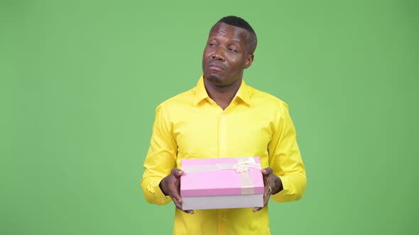 Young Happy African Businessman Thinking While Holding Gift Box