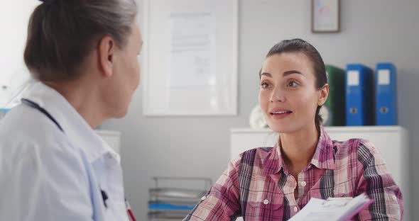 Happy Beautiful Young Woman Looking at Friendly Doctor During Visit in Hospital