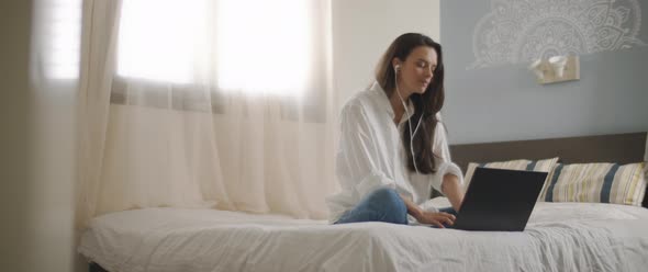 A young woman speaking to someone through earphones while working on her laptop