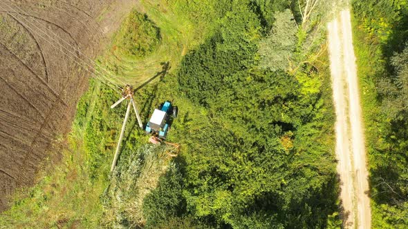 Elevated View Trees Trimming Using a Flail Hedge Cutter Attached to Blue Tractor Along the Side of