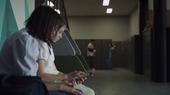 Two Serious Schoolgirls Scrolling Tablet in Hall