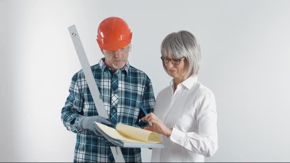 An Elderly Worker in a Helmet and a Female Engineer with a Tablet and a Level in Their Hands Discuss