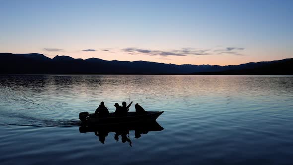 4 people sitting in fishing boat on a lake at dusk