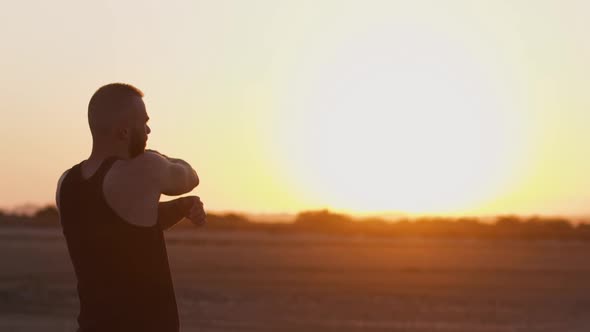 Sporty Man with Smartwatch Stretching Arms on Beach at Sunset