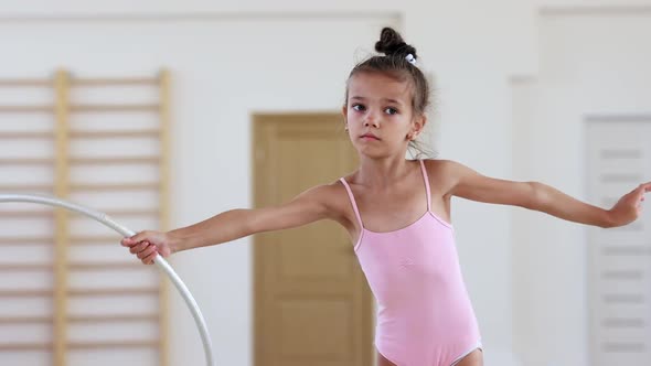 A Little Acrobatic Girl Twisting a Hoop in Her Hand in Ballet Studio