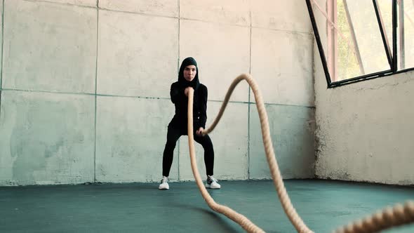 A strong arabian sports woman wearing national hijab is training with a battle of ropes