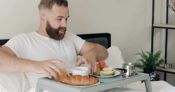 Handsome Bearded Man Sitting with Tray Full of Food on His Legs and Enjoing Morning, Happy Guy 