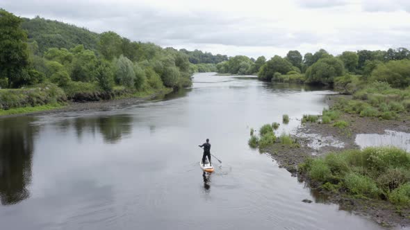 Lone man paddles SUP on small peaceful river in rural countryside